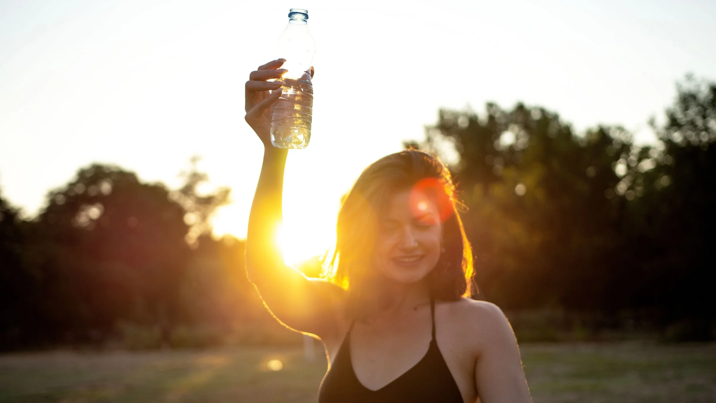 A person dancing in a park, holding a water bottle.