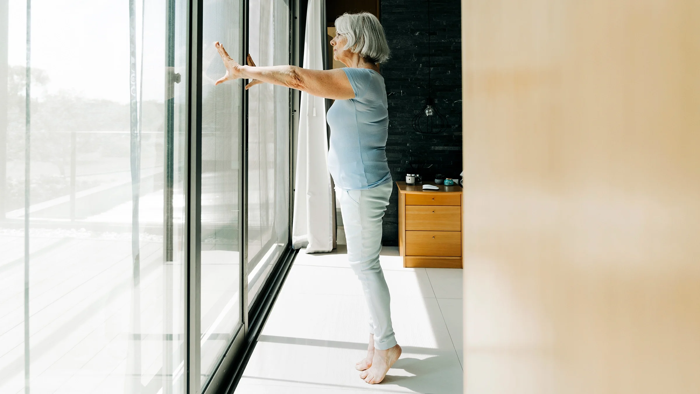 Senior woman doing heel lift exercise while standing on tiptoe in the bedroom.