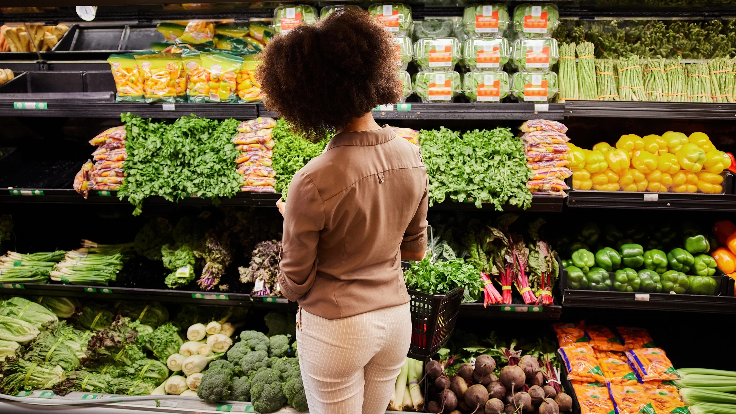 Woman standing at the produce selection at the grocery store. She has her back to the camera.