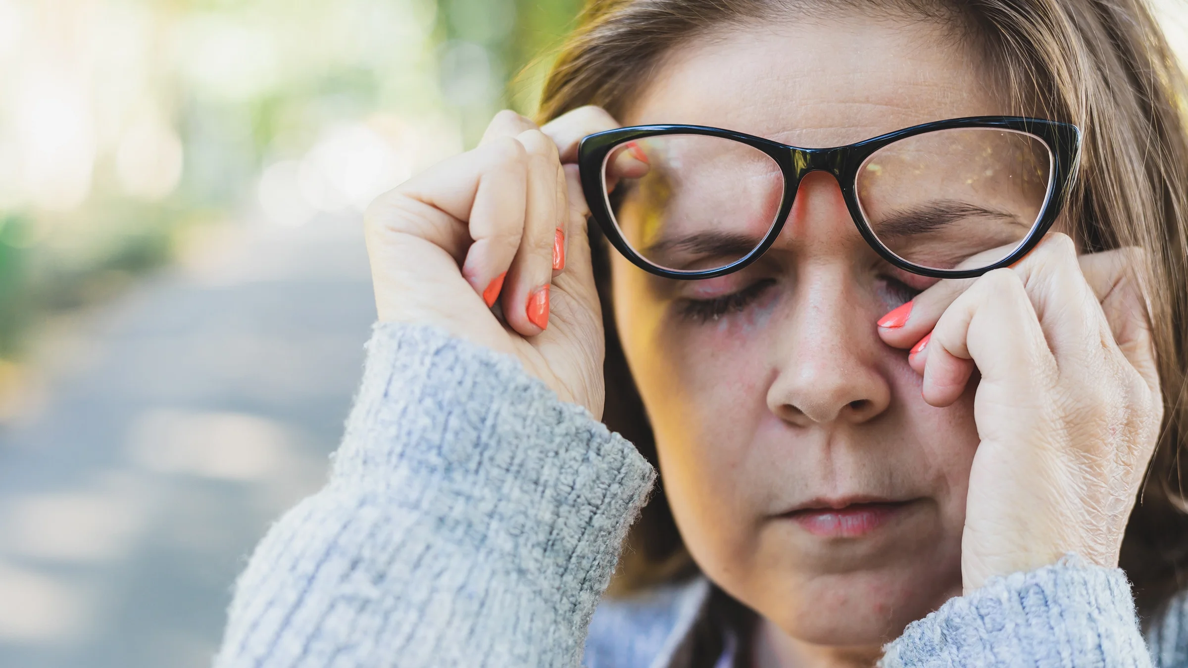 Close-up of a woman removing her glasses to rub her eye.