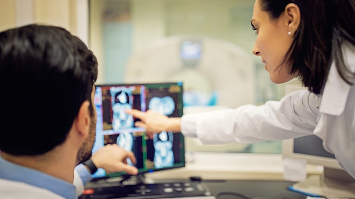 Doctor reviewing and pointing out areas of interest on a CT scan displaced on a computer screen.
