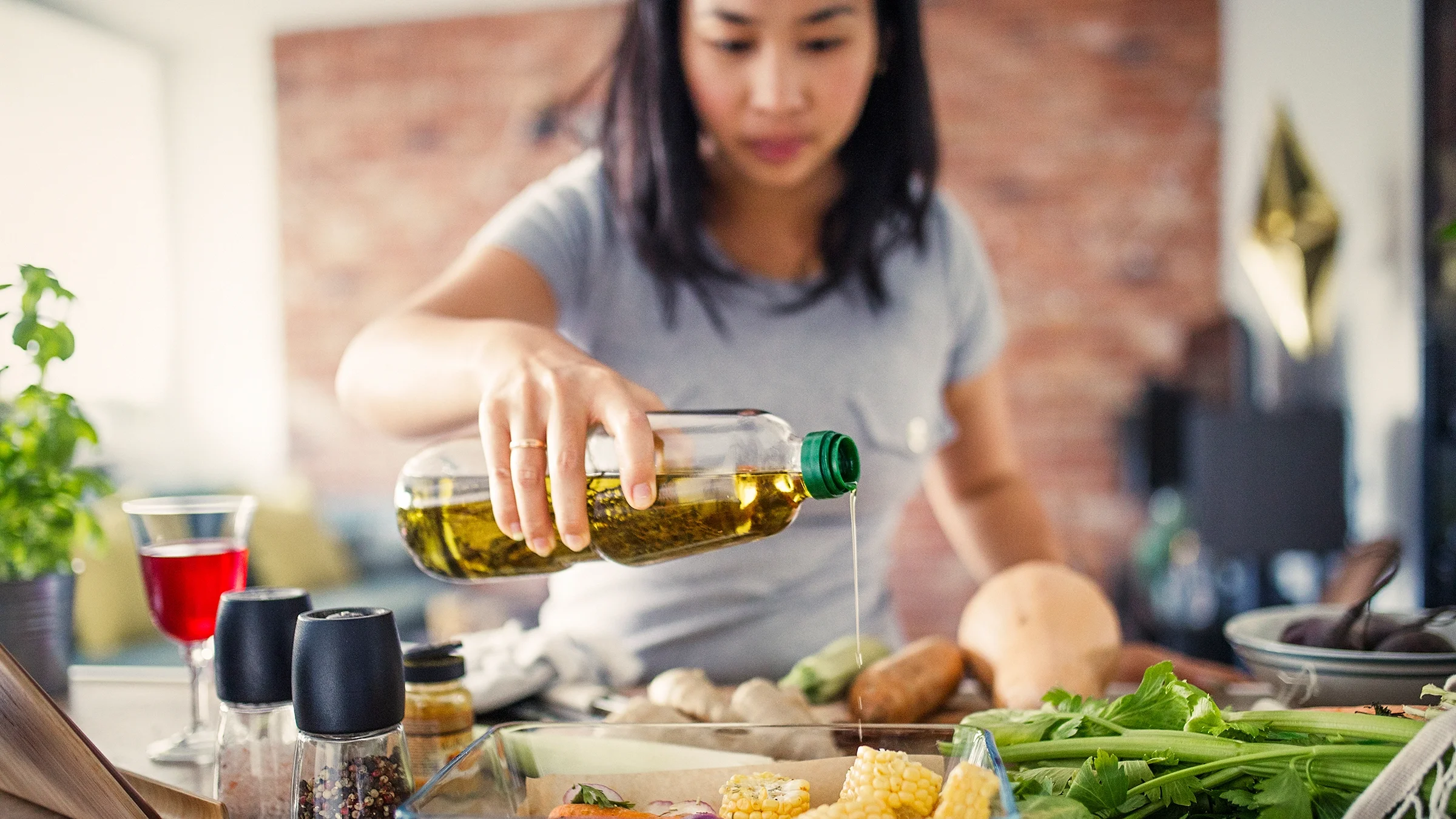 A woman pours olive oil over vegetables. 