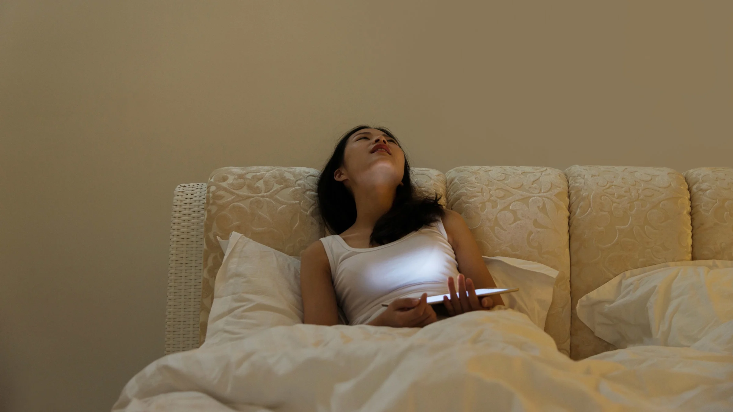 A person looking stressed out, using their laptop in bed.