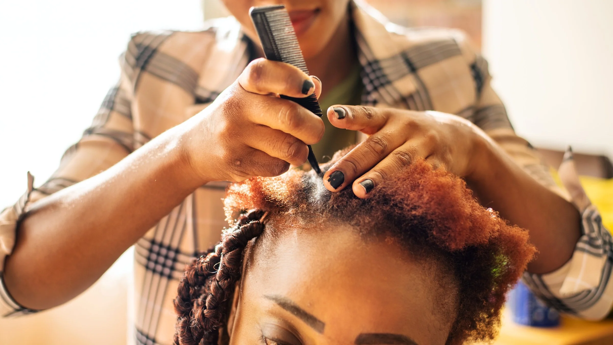 A hairstylist is braiding a client’s hair.