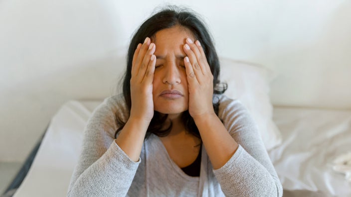 A person with a headache in bed, holding their face.