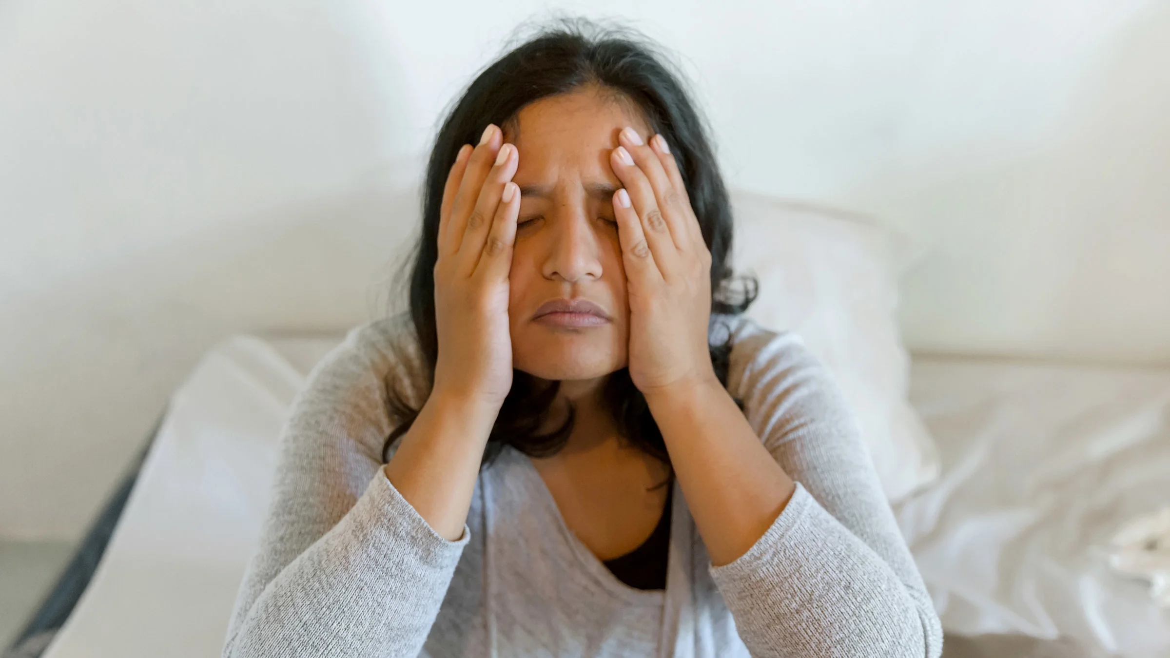 A person with a headache in bed, holding their face.