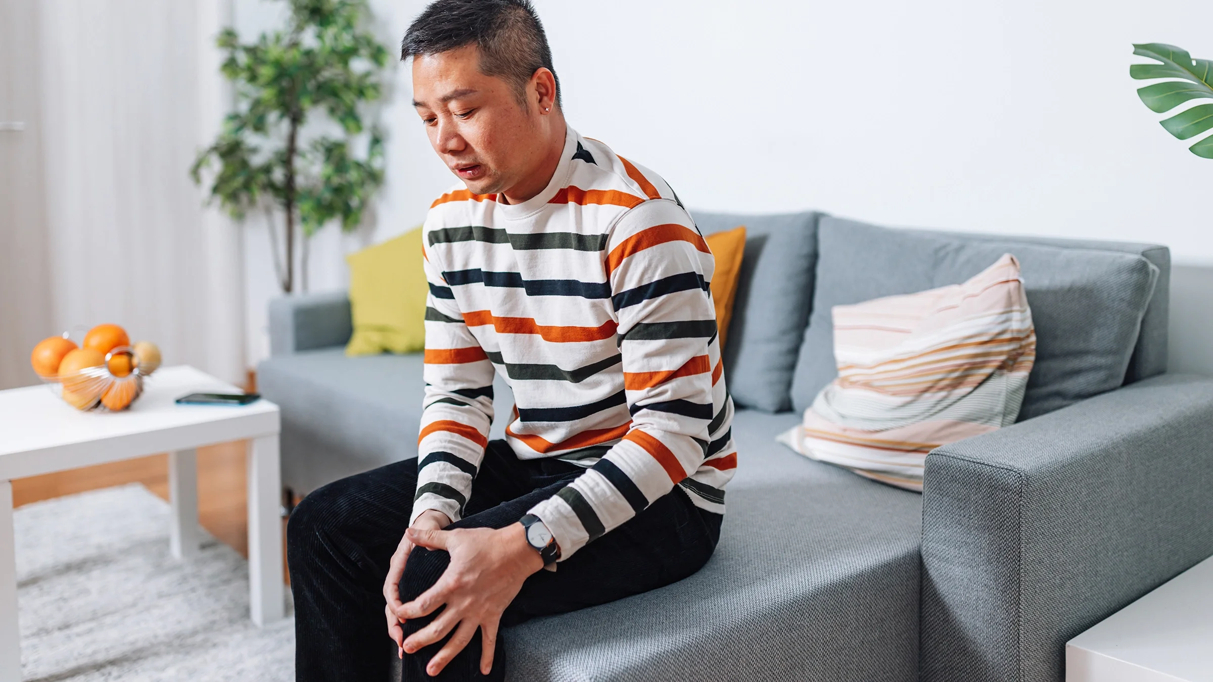 A person is sitting on a couch, holding their knee.