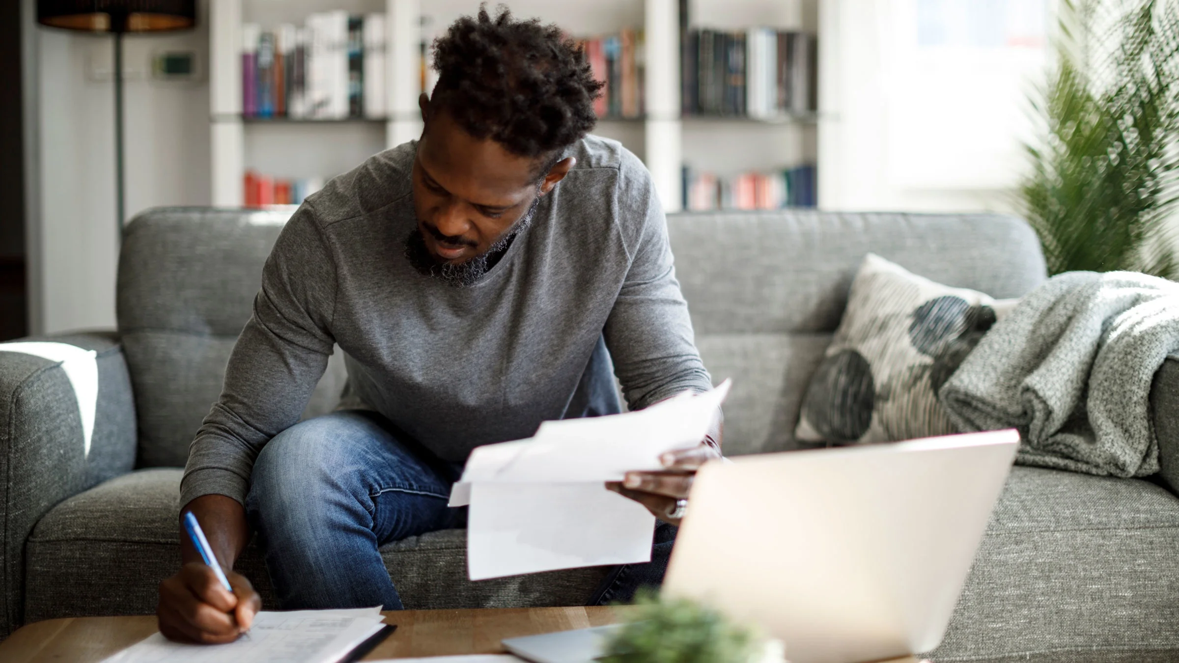 A man sits on a couch doing calculations on paper..