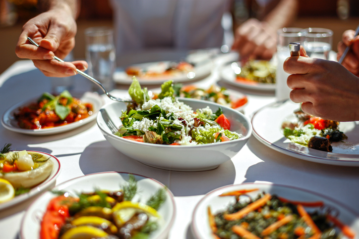 Close-up of a lunch table with Greek salads and Mediterranean food, someone is serving themselves salad.
