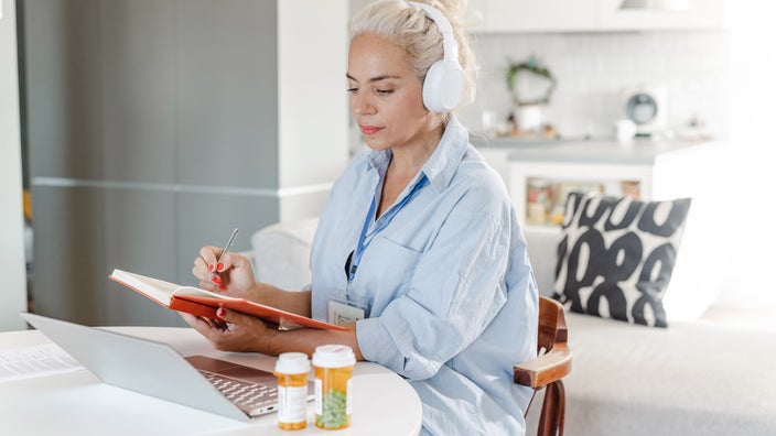 A psychiatrist taking notes in a telehealth session, at a desk with pill bottles.