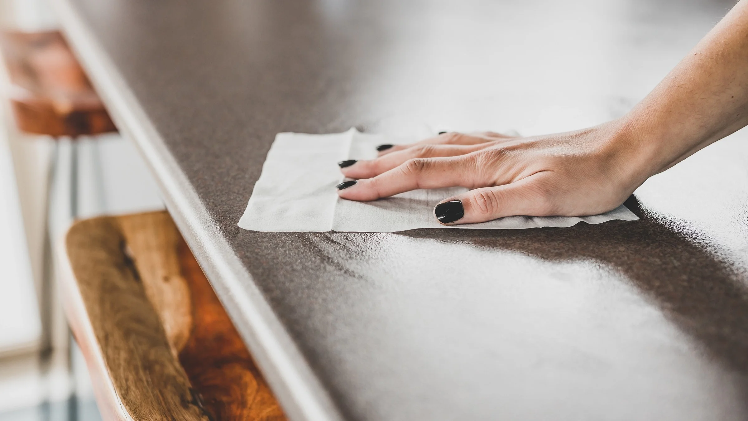 Close-up of a woman's hand using a Clorox wipe to wipe down a kitchen counter.