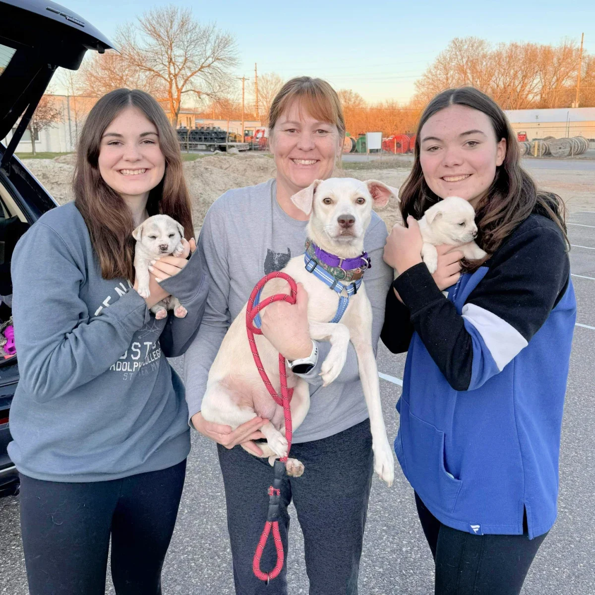Janelle Percy and her two daughters, Skylar and Peyton, are pictured standing next to a car holding dogs.