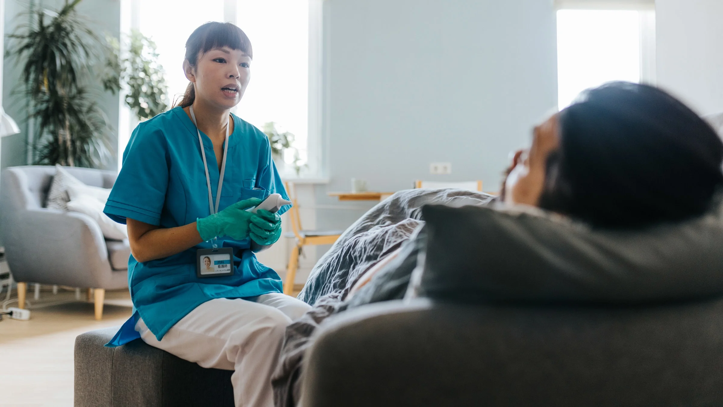 Nurse holding a thermometer and talking to a patient who is in bed.
