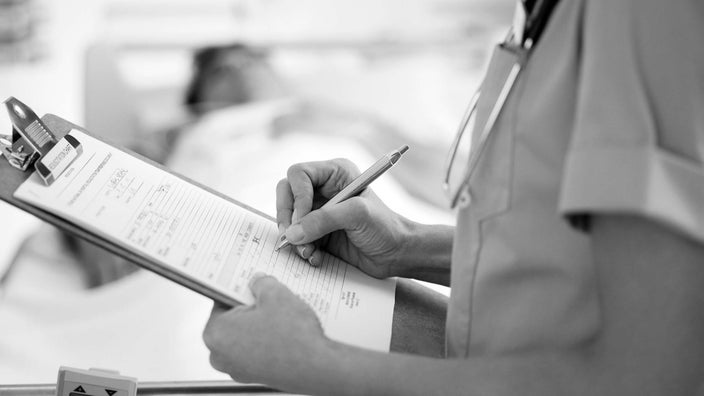 A black and white close-up image of a nurse filling out a form on her clipboard.