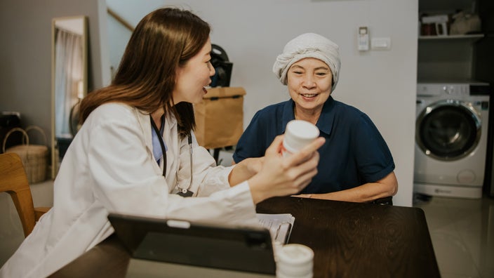 A doctor explaining a pill bottle to a cancer patient during a home visit.