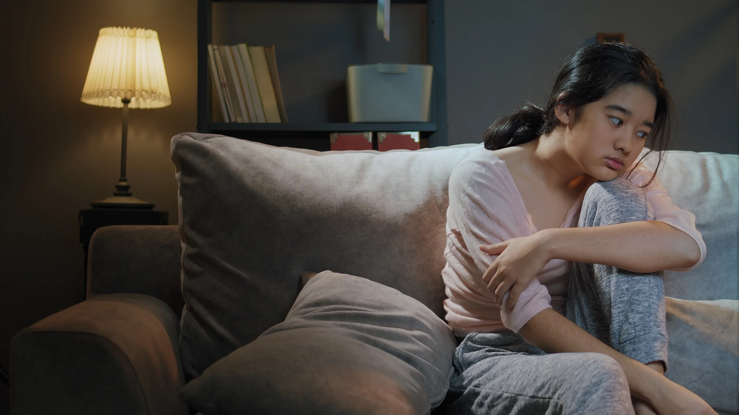 Young woman staying up late on the couch because she can't sleep. She has her chin resting on her knee.