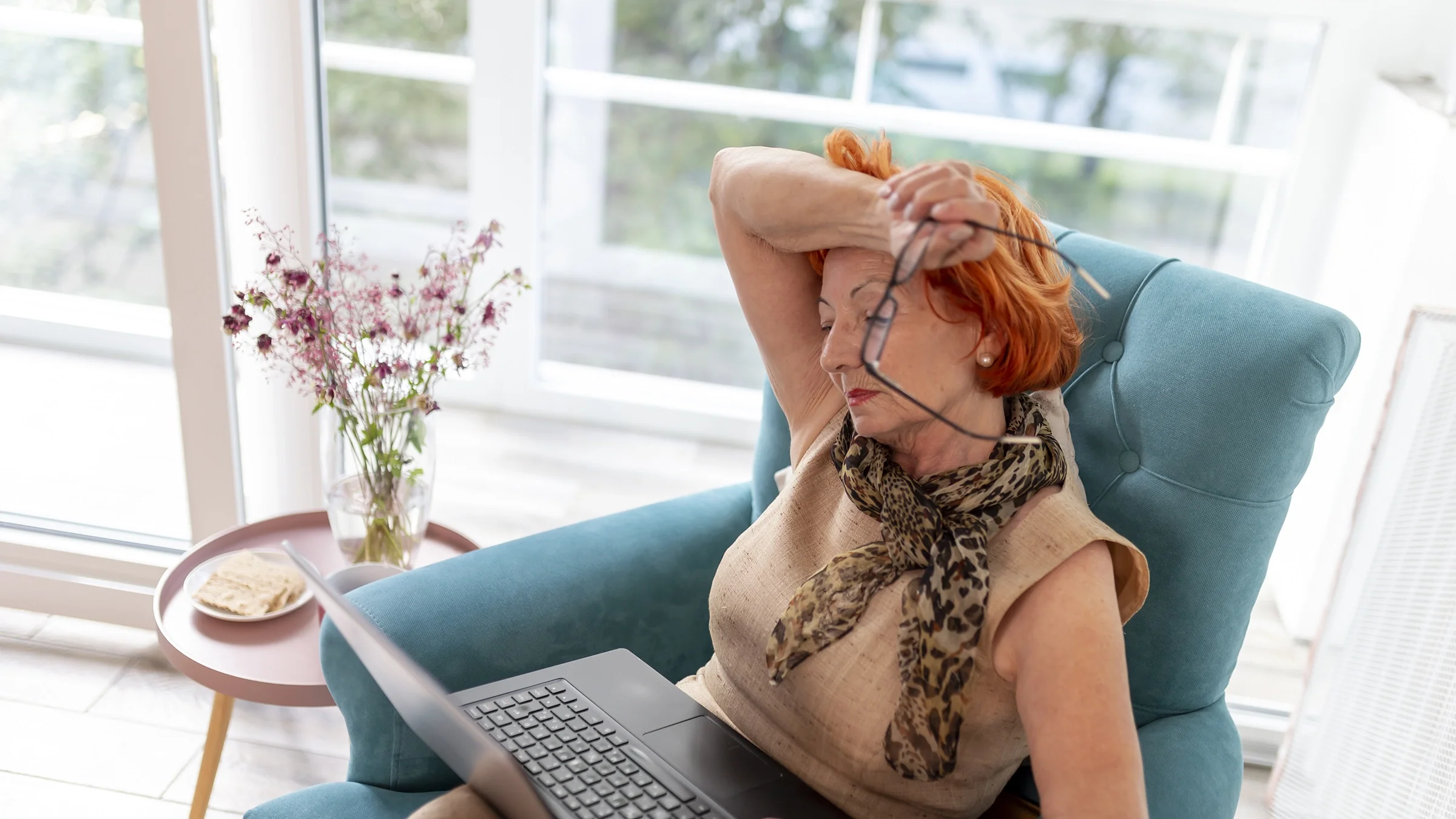 A woman deals with a hot flash while using her laptop at home.