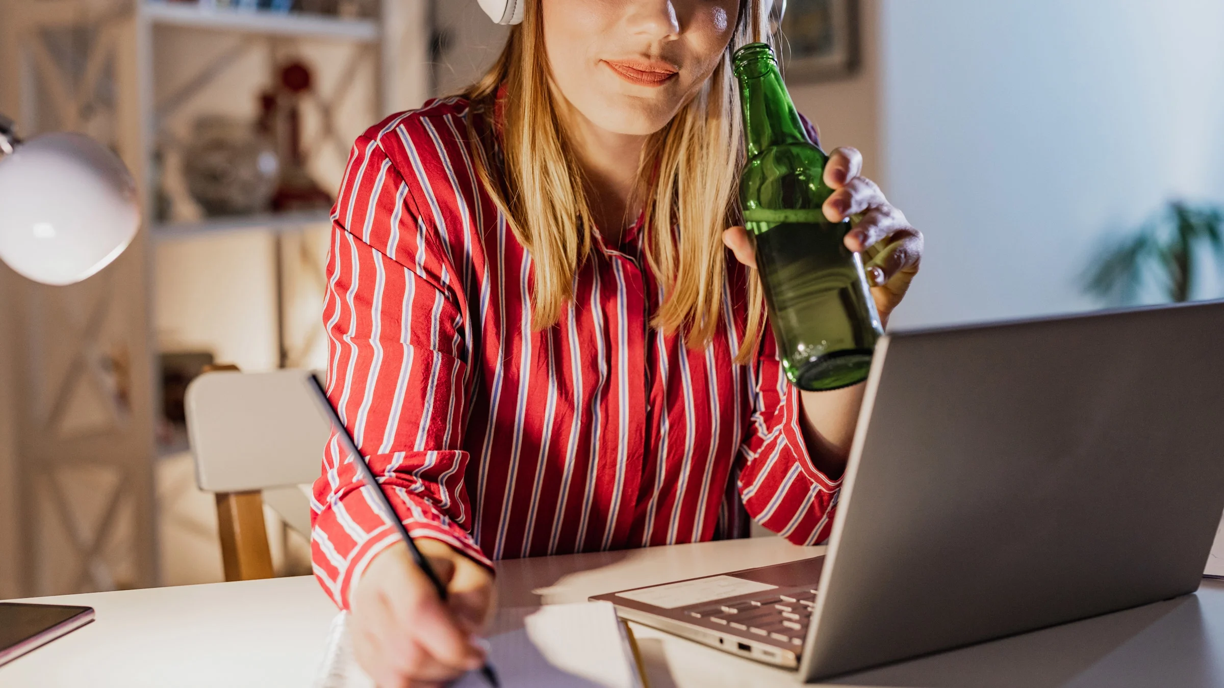 A person working on their laptop with a beer in one hand.