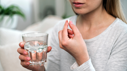 A woman is holding a white pill and a glass of water.
brizmaker/iStock via Getty Images Plus