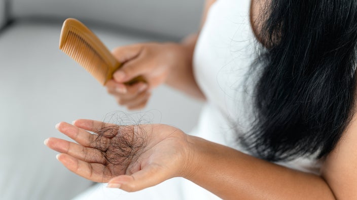A woman holds strands of hair in one hand and a comb in the other. 
