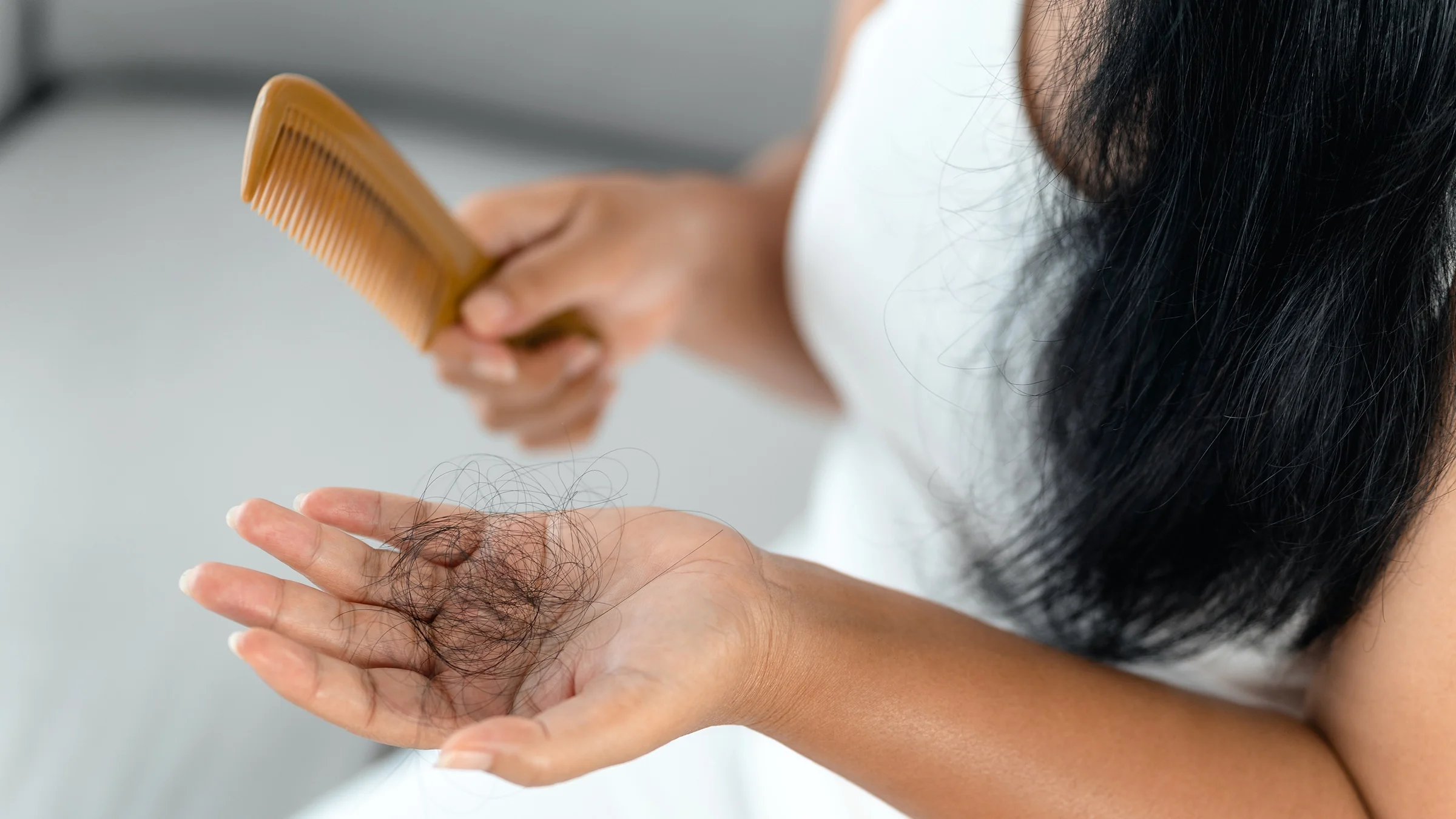 A woman holds strands of hair in one hand and a comb in the other. 