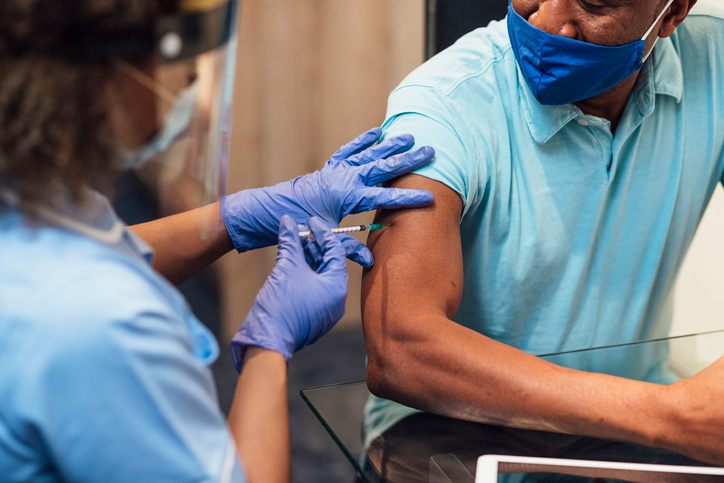 Close-up of a Black man getting the COVID-19 vaccine administered by a nurse in blue medical gloves.