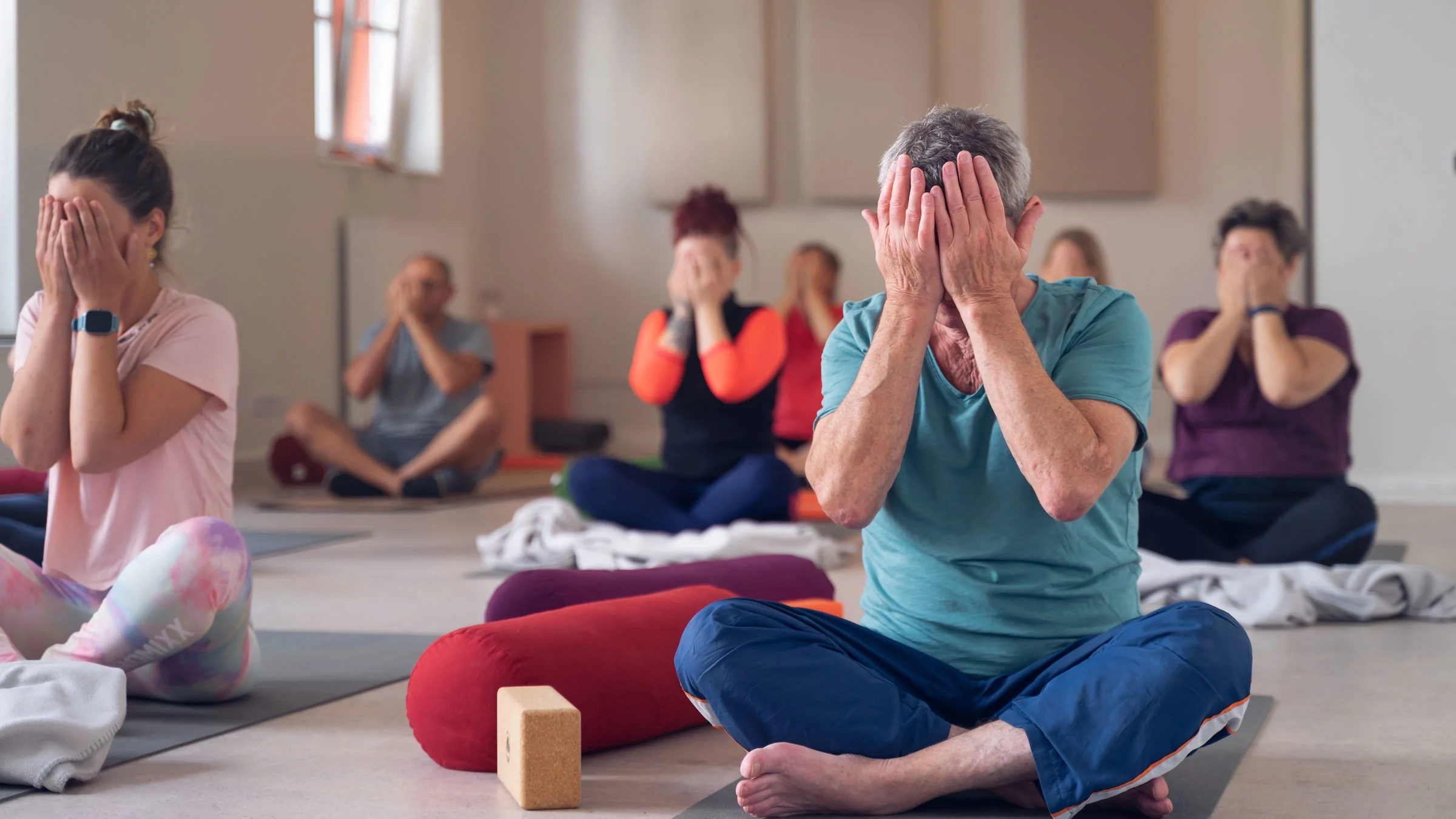 Group of people covering the eyes while sitting on the floor in a yoga class.