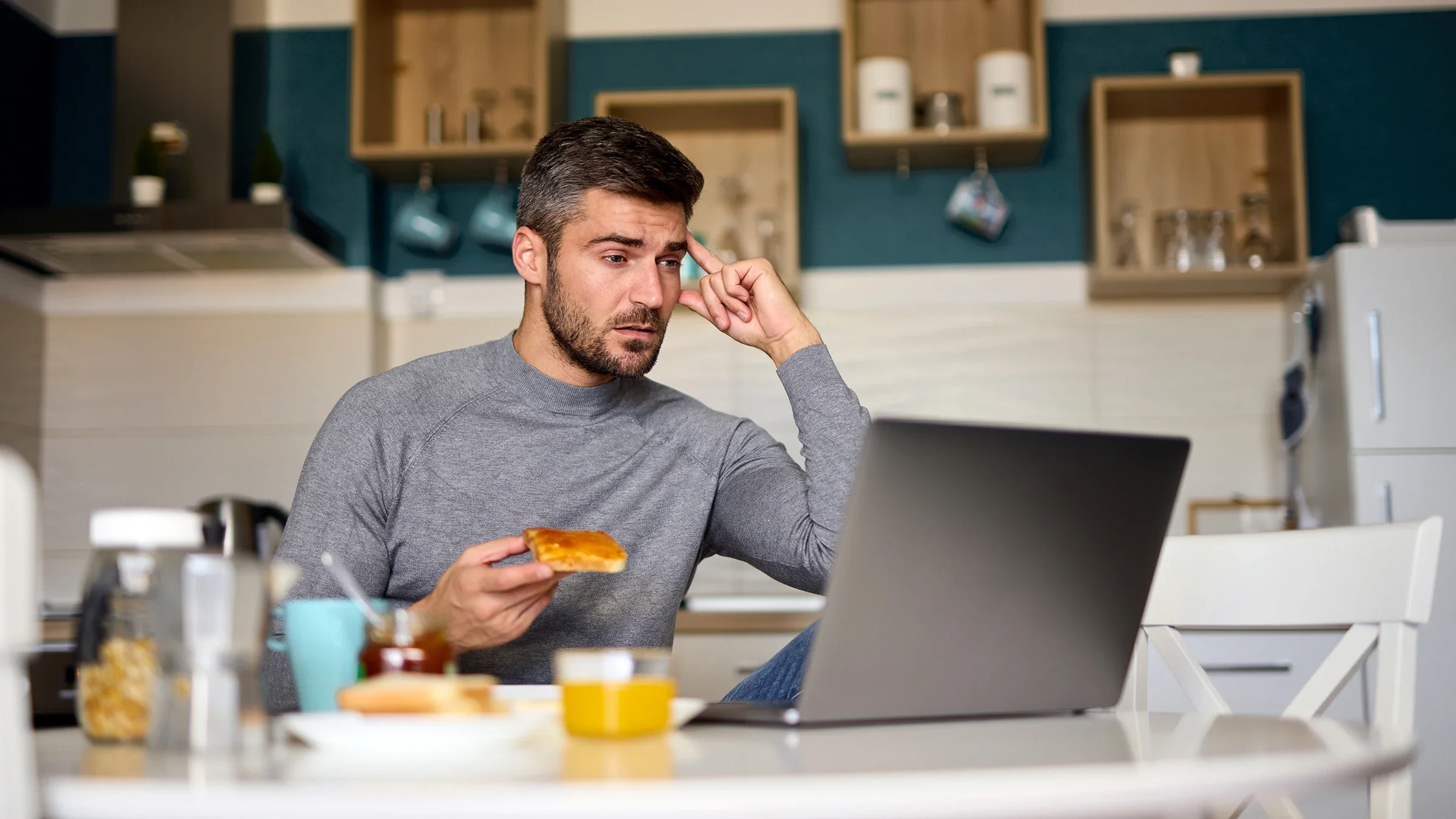 A man is on a video call while having breakfast in his dining room. 
EmirMemedovski/E+ via Getty Images