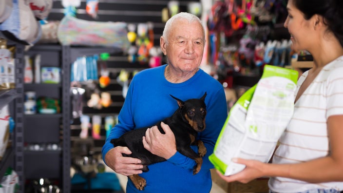 A senior man chooses dog food in a pet shop.