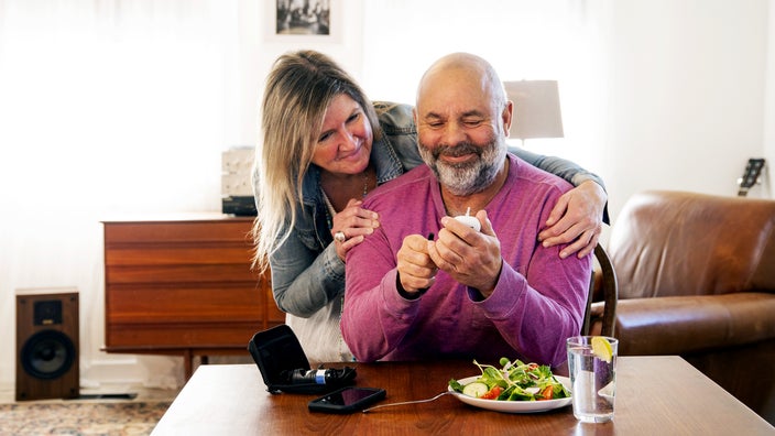 A man checks his blood sugar at home with his wife.