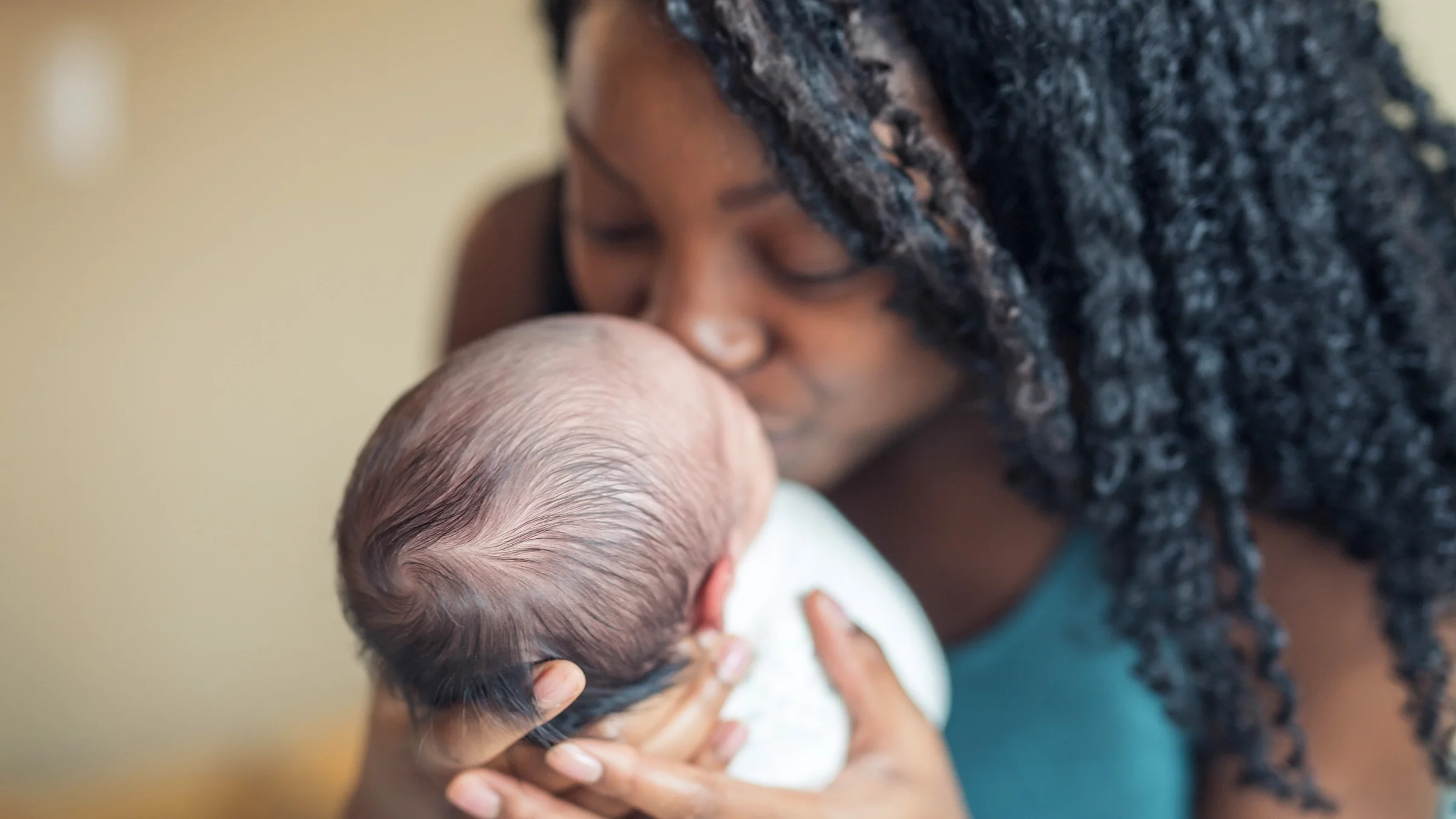 Portrait of a mother kissing her newborn.