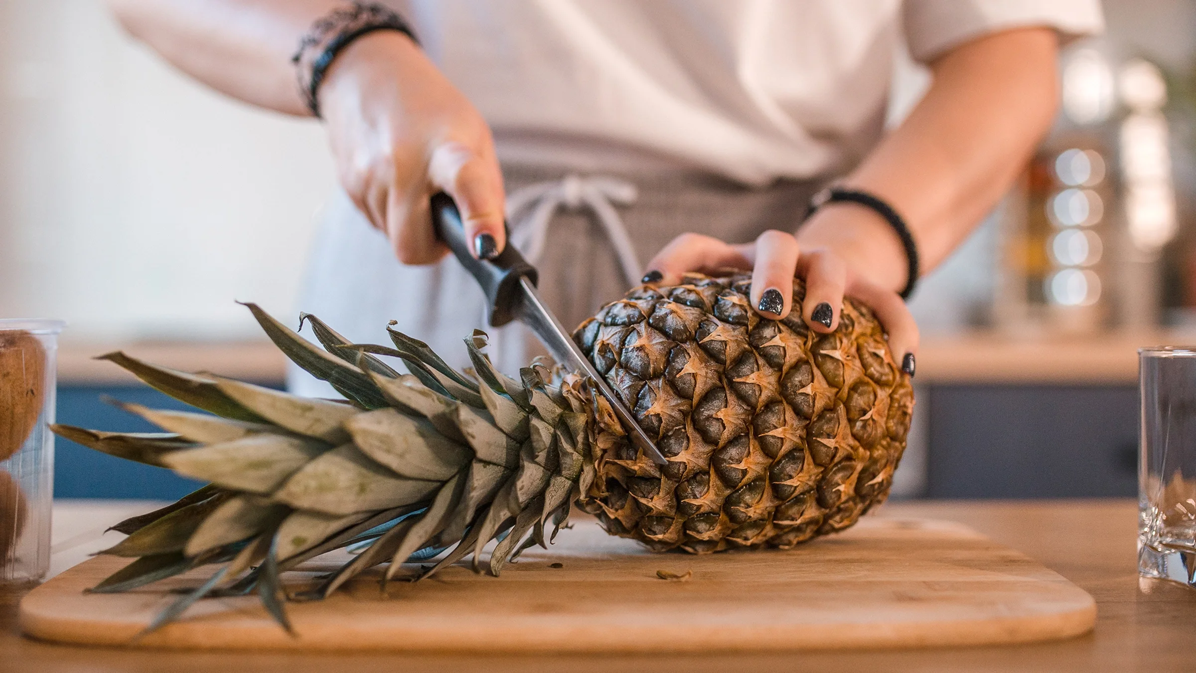 Close-up of woman cutting pineapple in the kitchen.