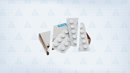 Light blue-gray background with texture and warning sign pattern. In the center is a box and two blister packs of pills cut into thirds. 
GoodRx Health
