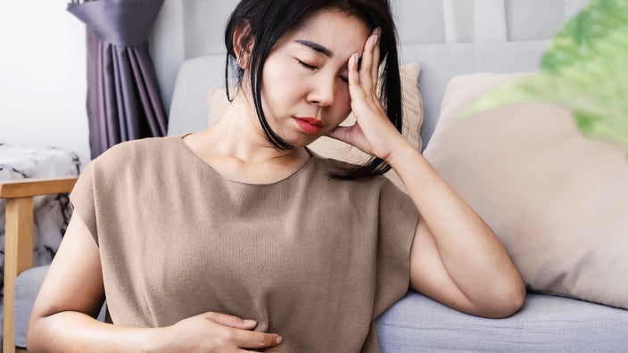 A woman is holding her head in pain with digestion symptoms.