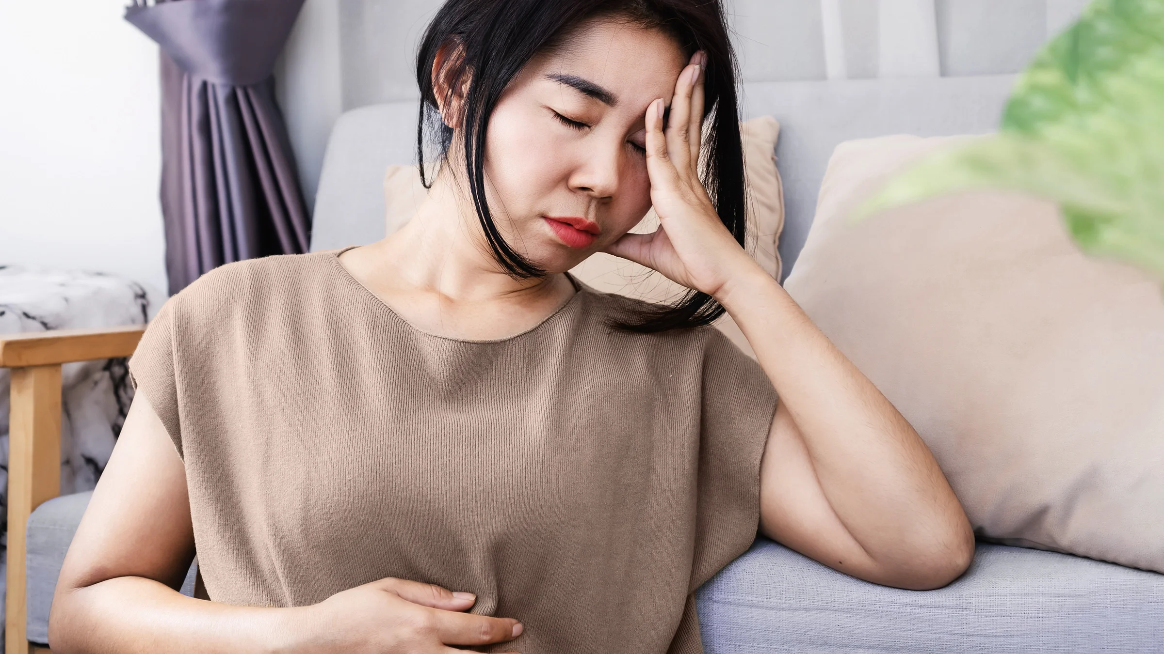 A woman is holding her head in pain with digestion symptoms.
