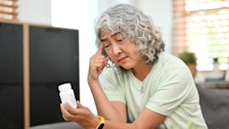 A woman looks worried while holding a medication bottle and sitting on her couch at home.
PrathanChorruangsak/iStock via Getty Images Plus