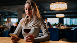 A person holding a wine glass while searching information on their phone.
dikushin/iStock via Getty Images Plus 
