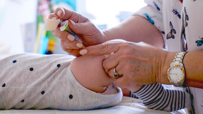 Close-up of a pediatrician's hand giving a baby a vaccine shot in their thigh.