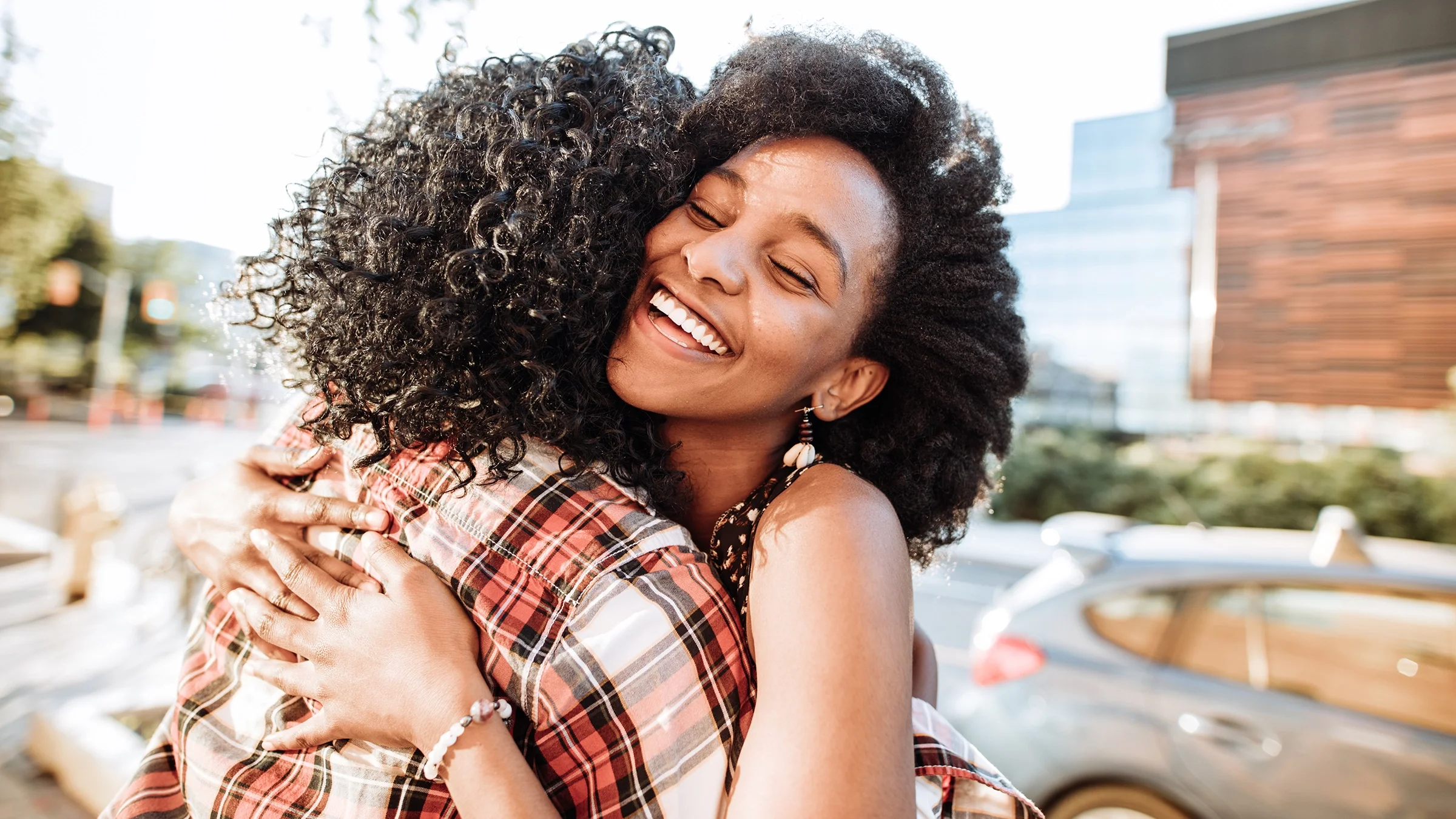 Friends hugging and smiling outdoors in the sunshine.