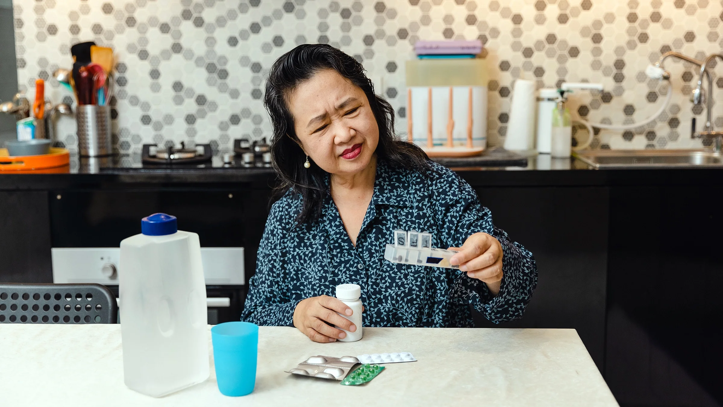 A woman studies her pill box at her kitchen table.