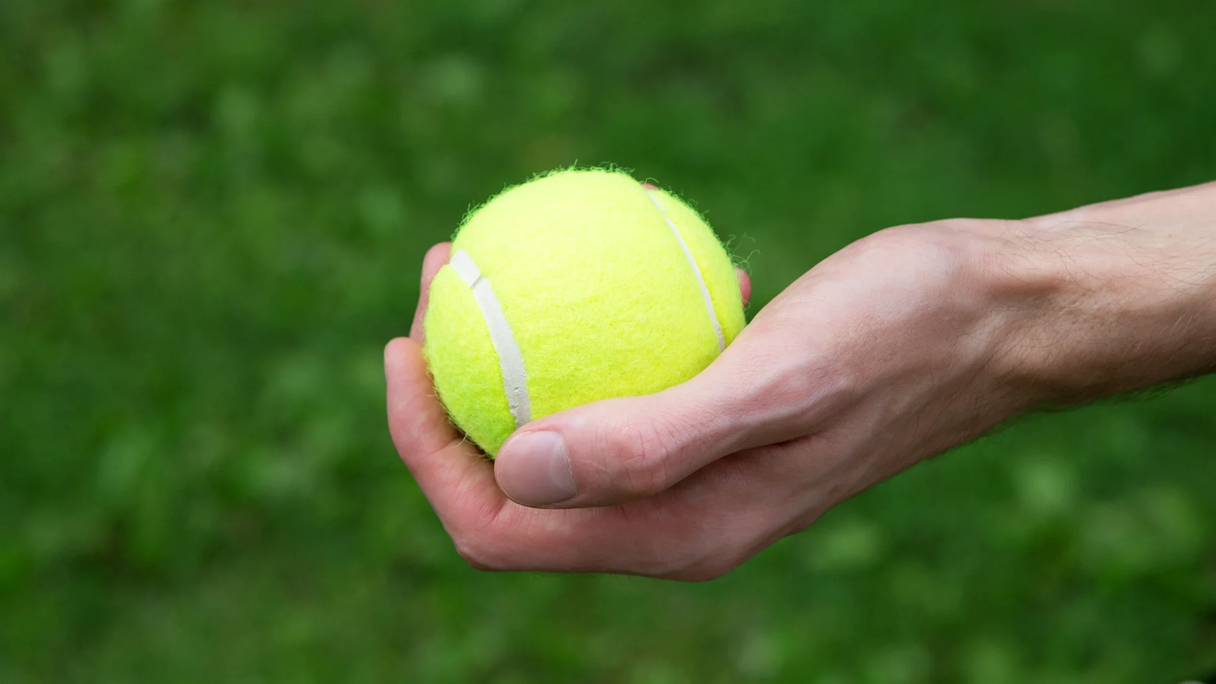 A close-up of a hand squeezing a tennis ball is shown.