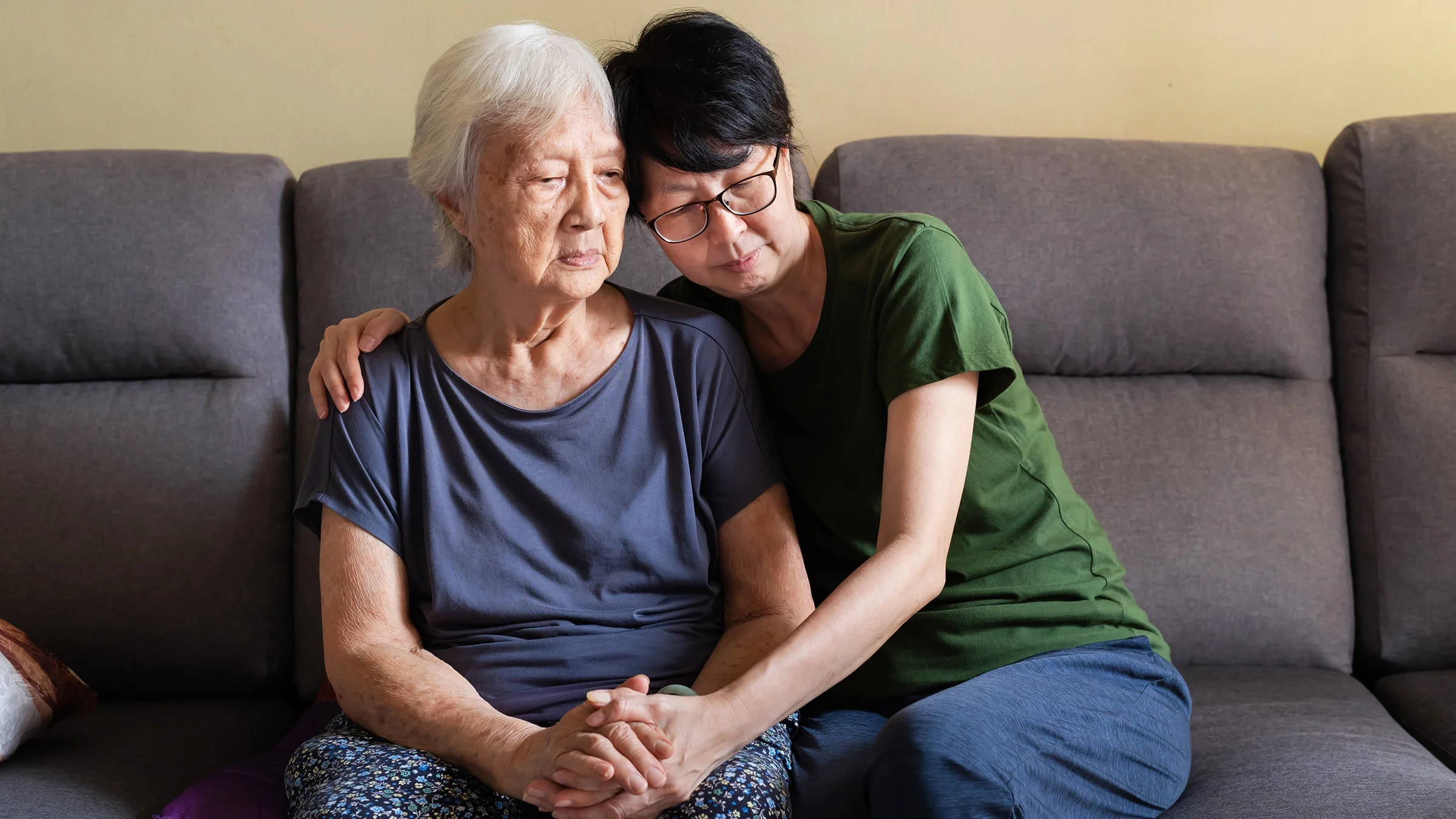 A woman hugs her elderly mother on the couch.