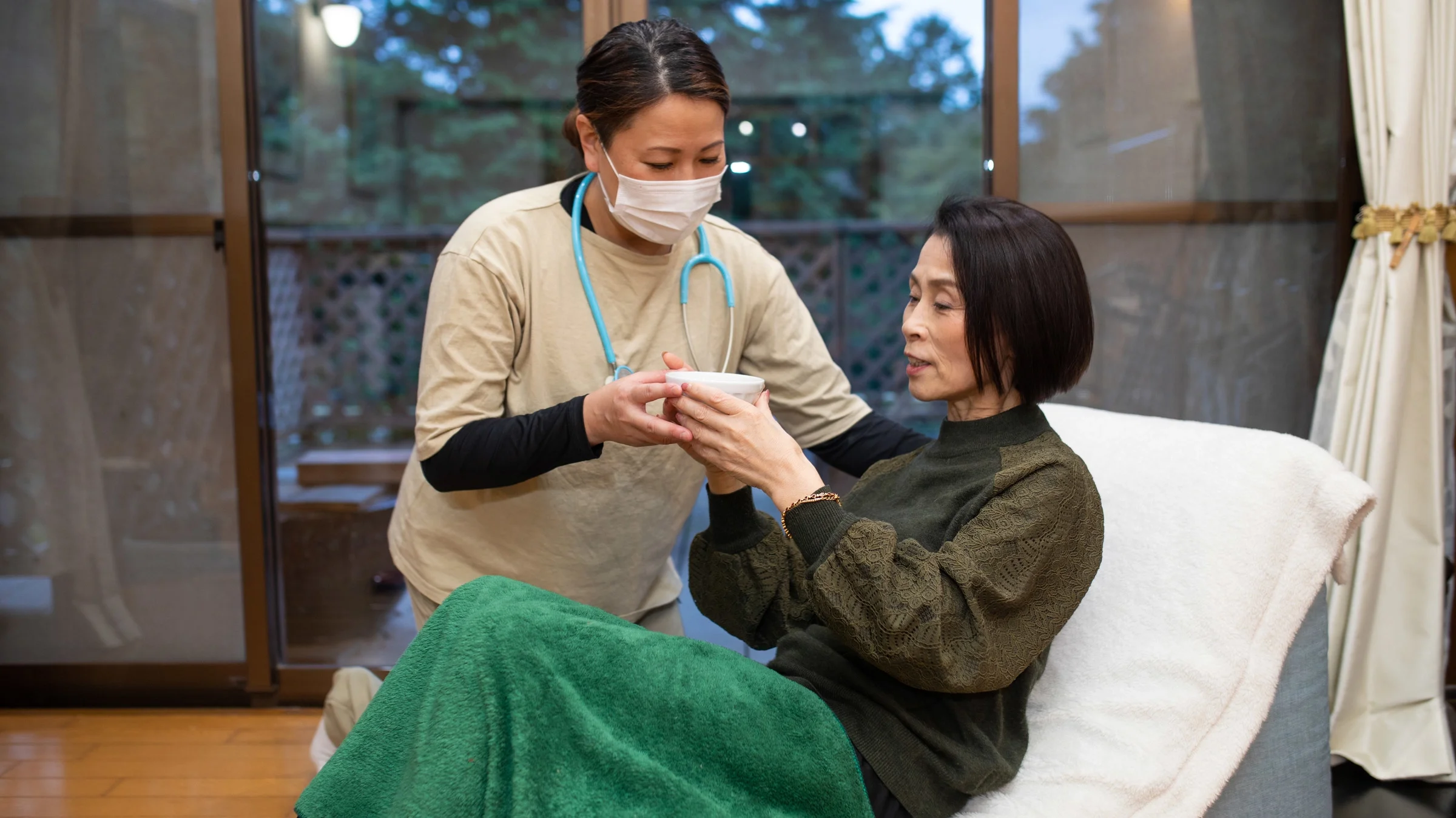 An at-home caretaker offering tea to senior patient