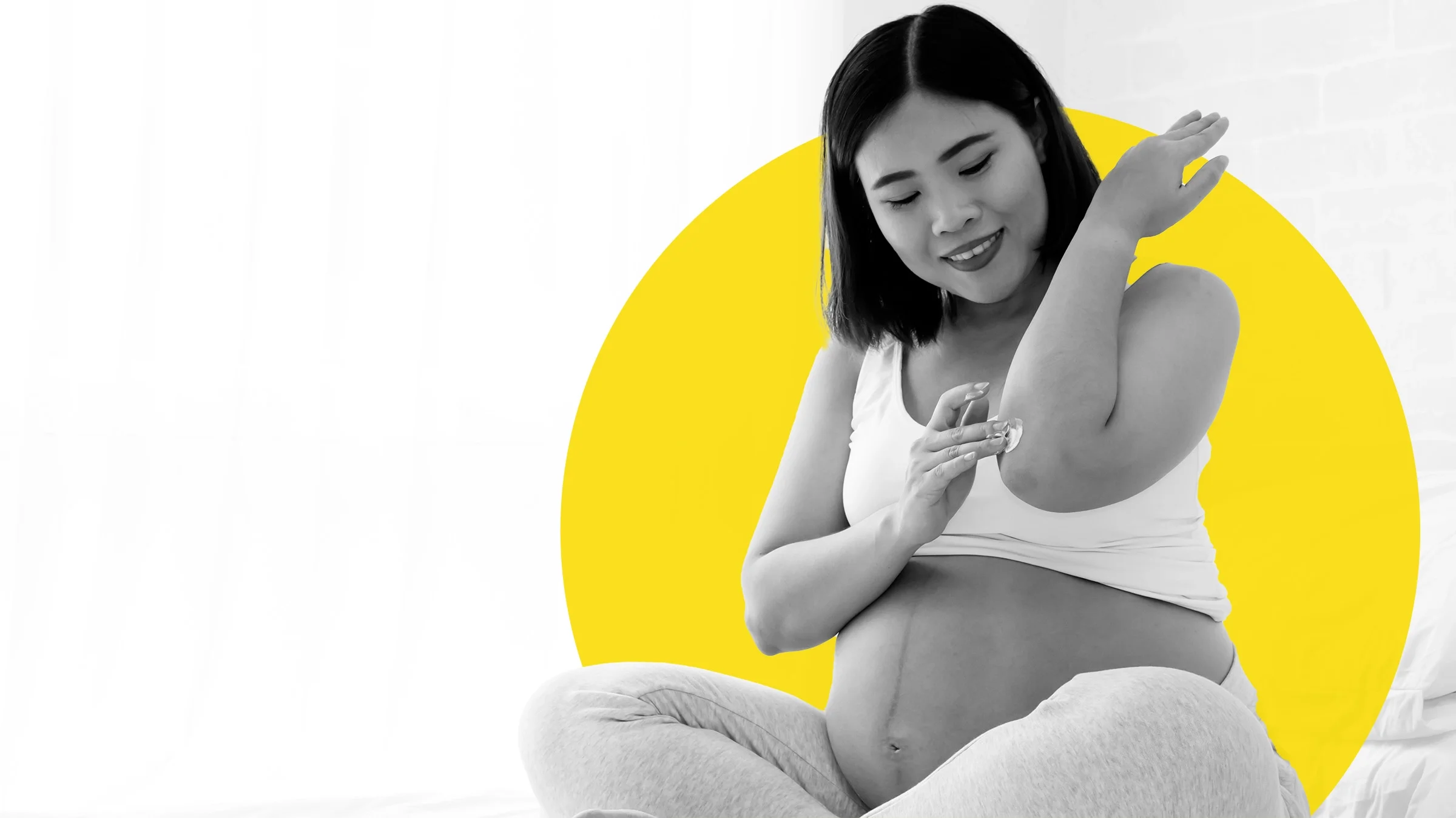 Black and white image of a pregnant woman sitting cross legged applying cream to her elbow. There is an added graphic yellow circle behind her.