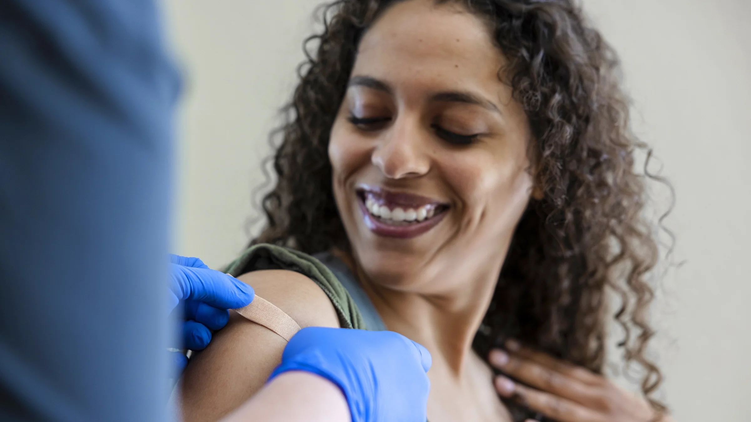 Close-up of a woman getting a shot from a nurse wearing blue medical gloves and putting a band-aid on the woman's arm.