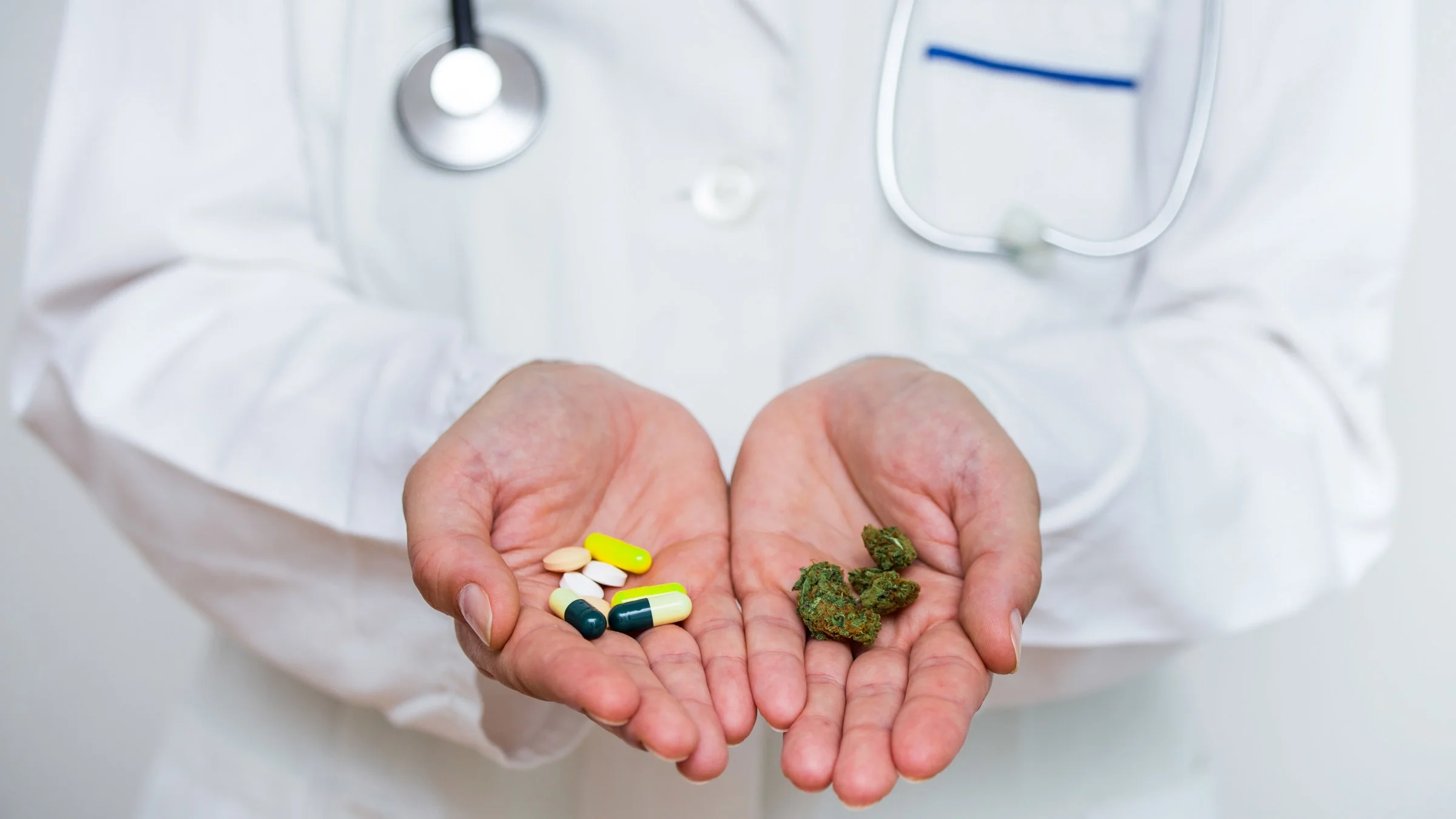 A doctor holding cannabis in one hand and pills in the other.