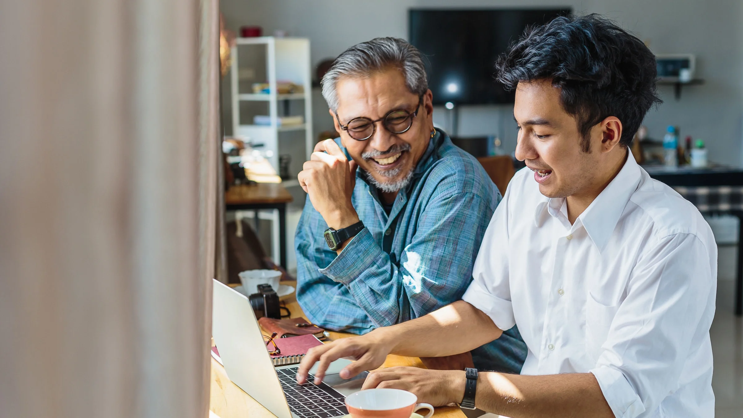 A father and son are using a laptop at home.
