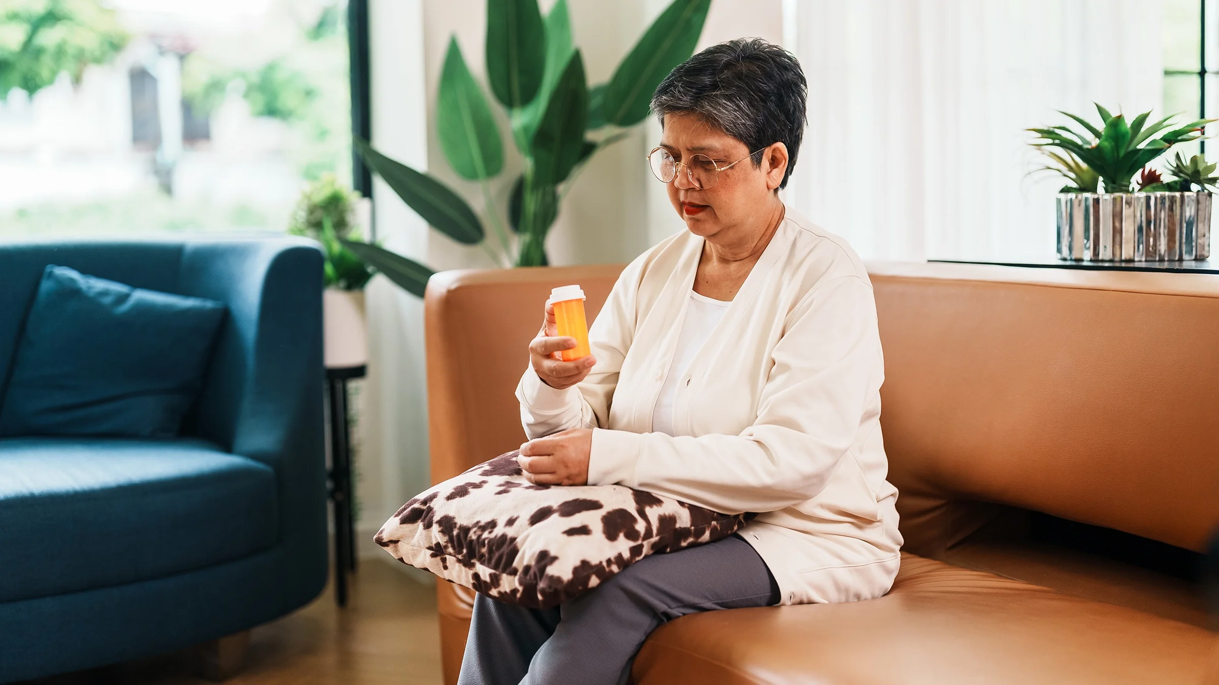 A woman examines her medication bottle as she sits on her sofa at home.