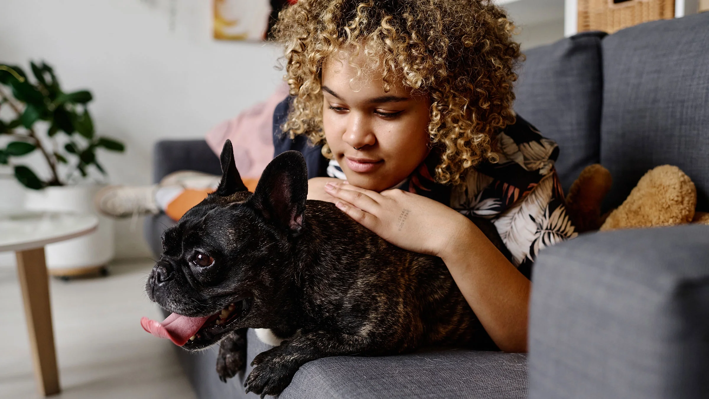 Woman lying on a sofa with a panting French bulldog.