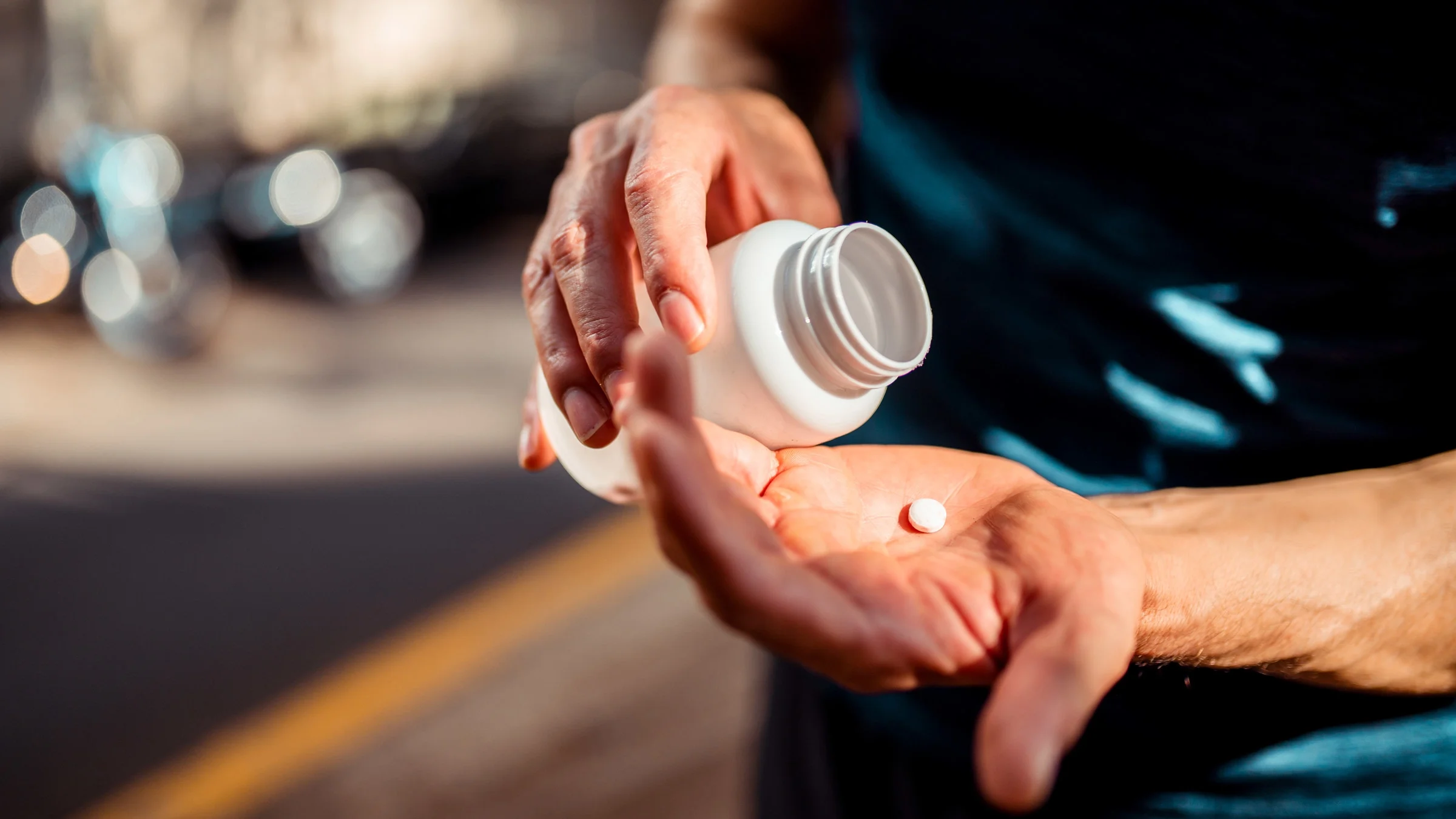 Close-up of a man’s hands pouring a pill from a bottle into his palm. 